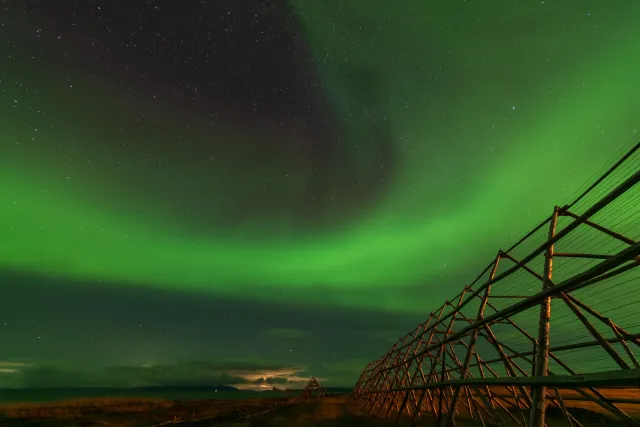 Polarlichter über den Trocknungsgestellen für FisPolarlichter über den Trocknungsgestellen für Fisch in Ekkerøy mit aufgehendem Mondch in Ekkerøy